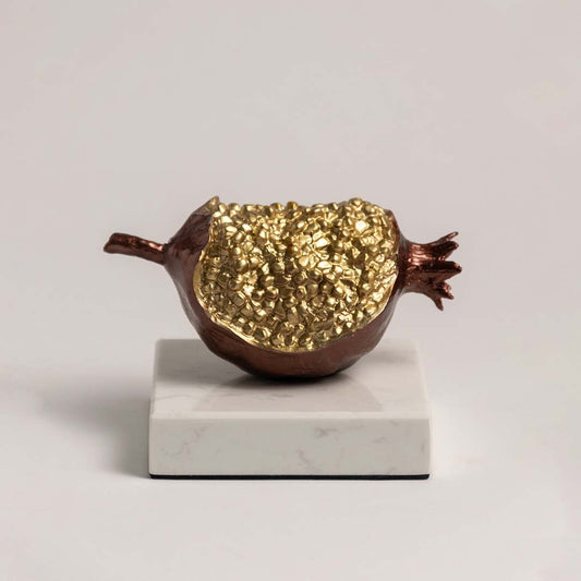 Elegant golden pomegranate sculpture on marble base displayed against plain white background.