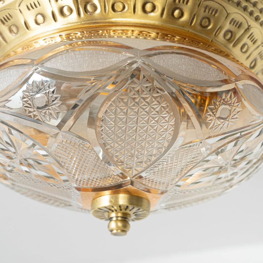 Detailed closeup of vintage ceiling light showing brass rim and intricate crystal cut glass pattern for elegant decor.