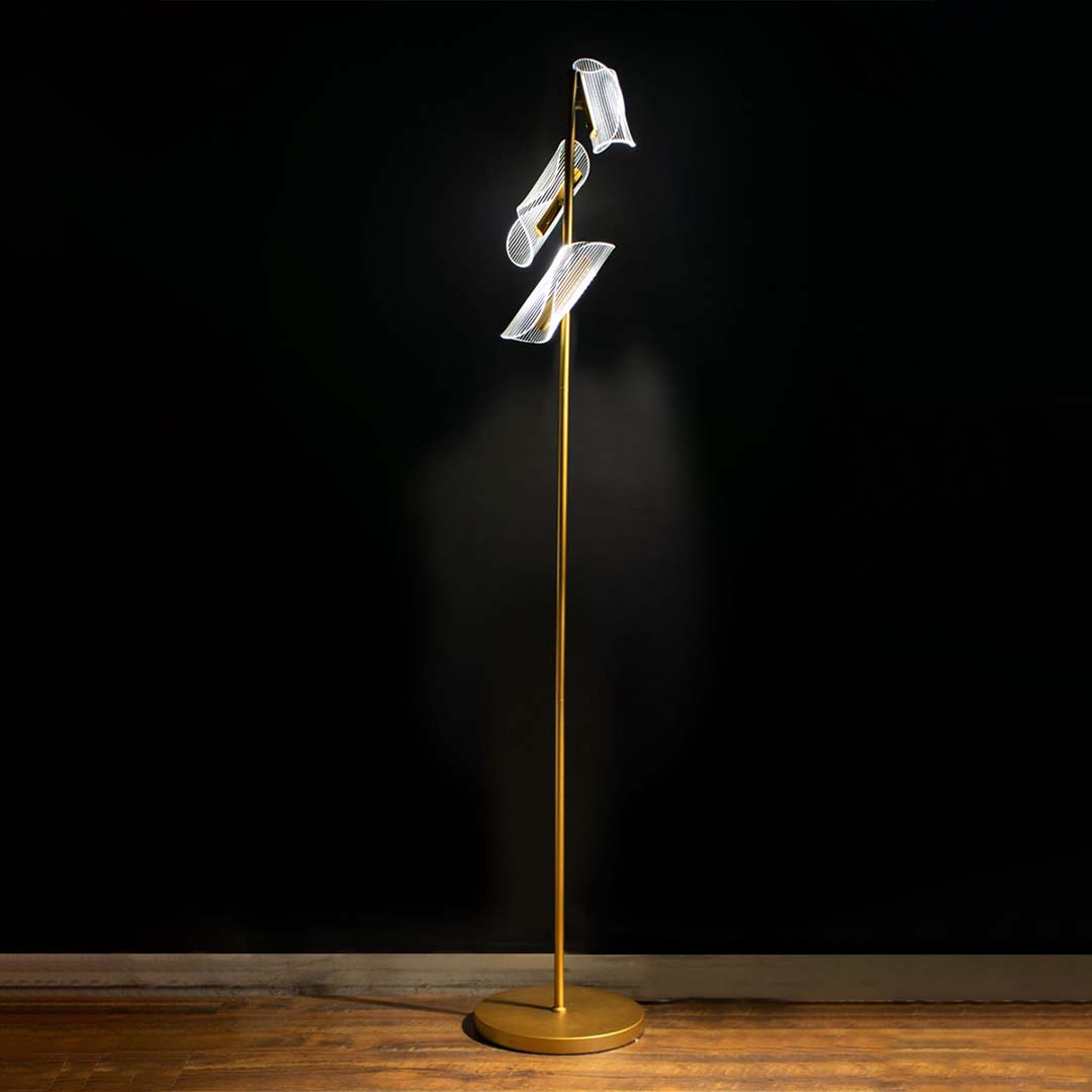 Artistic gold floor lamp displayed with light on against a dark backdrop enhancing its glowing acrylic panels and modern sculptural silhouette.