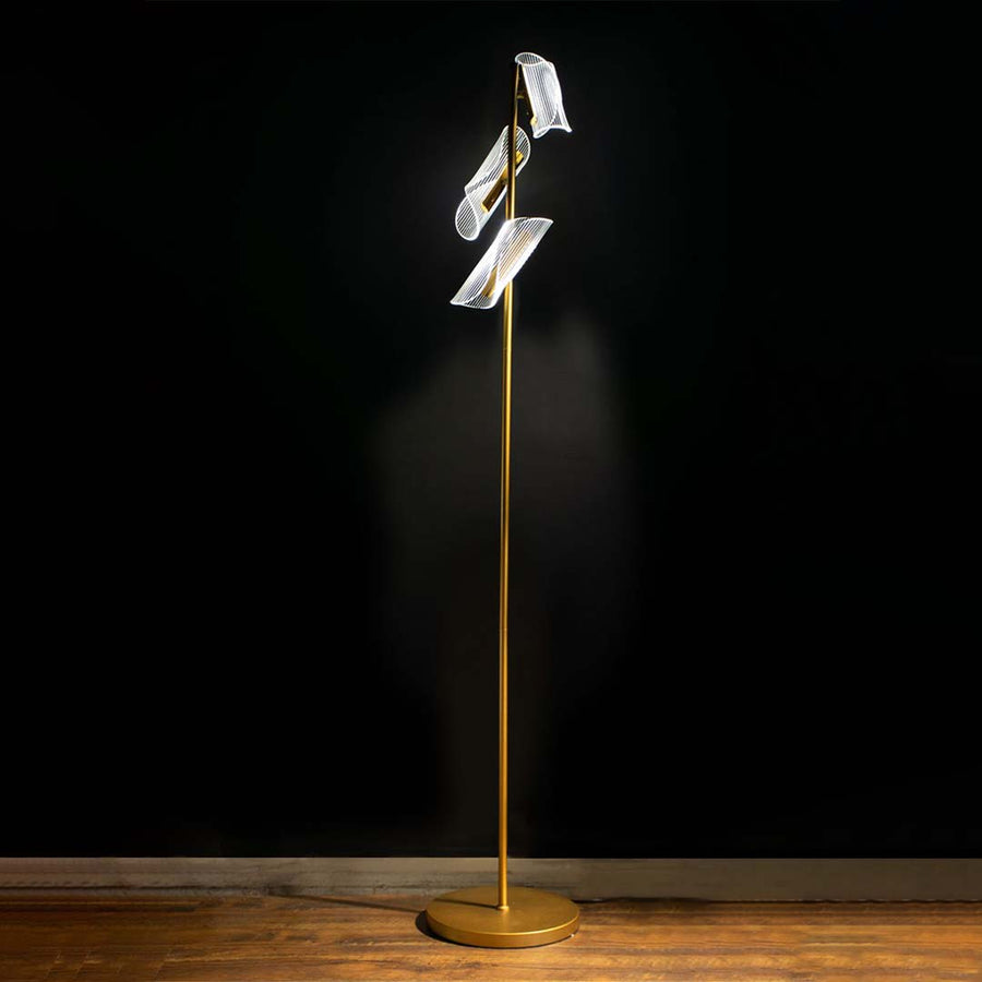 Artistic gold floor lamp displayed with light on against a dark backdrop enhancing its glowing acrylic panels and modern sculptural silhouette.