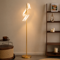 Modern gold brass tall floor lamp featuring three clear glass loop shades illuminated beautifully in a living room.