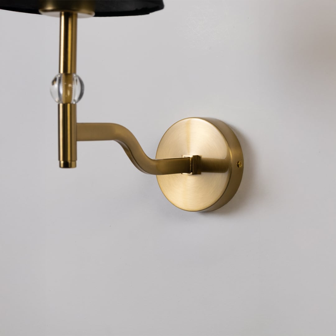 Closeup of gold metal wall light with black fabric shade and crystal accent showing refined detailing for elegant modern indoor lighting.