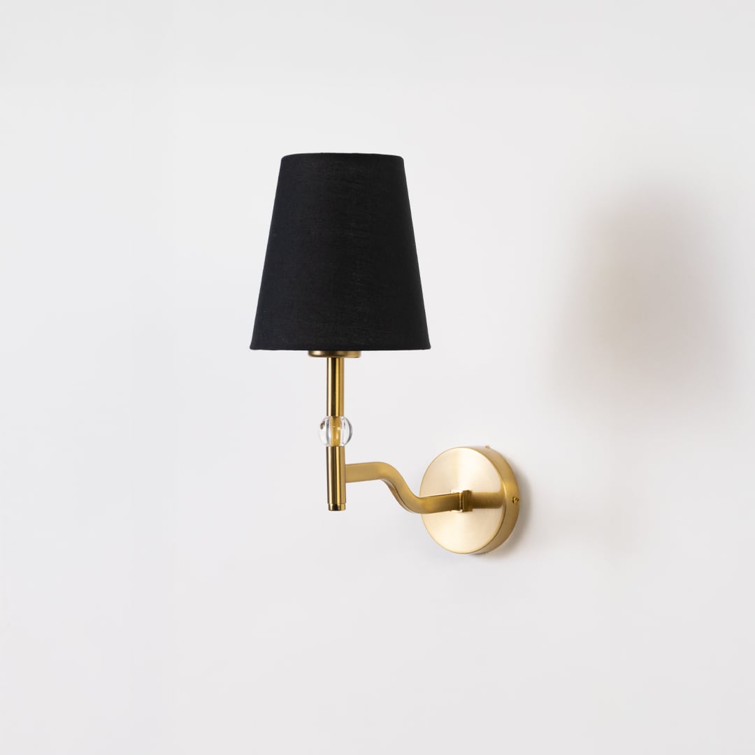 Gold metal wall light with black fabric shade on a bright white background with light off highlighting its sleek modern curved arm design.