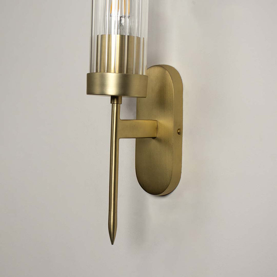 Modern brass metal wall light with clear glass cylinder shade for elegant bedroom and hallway decor.