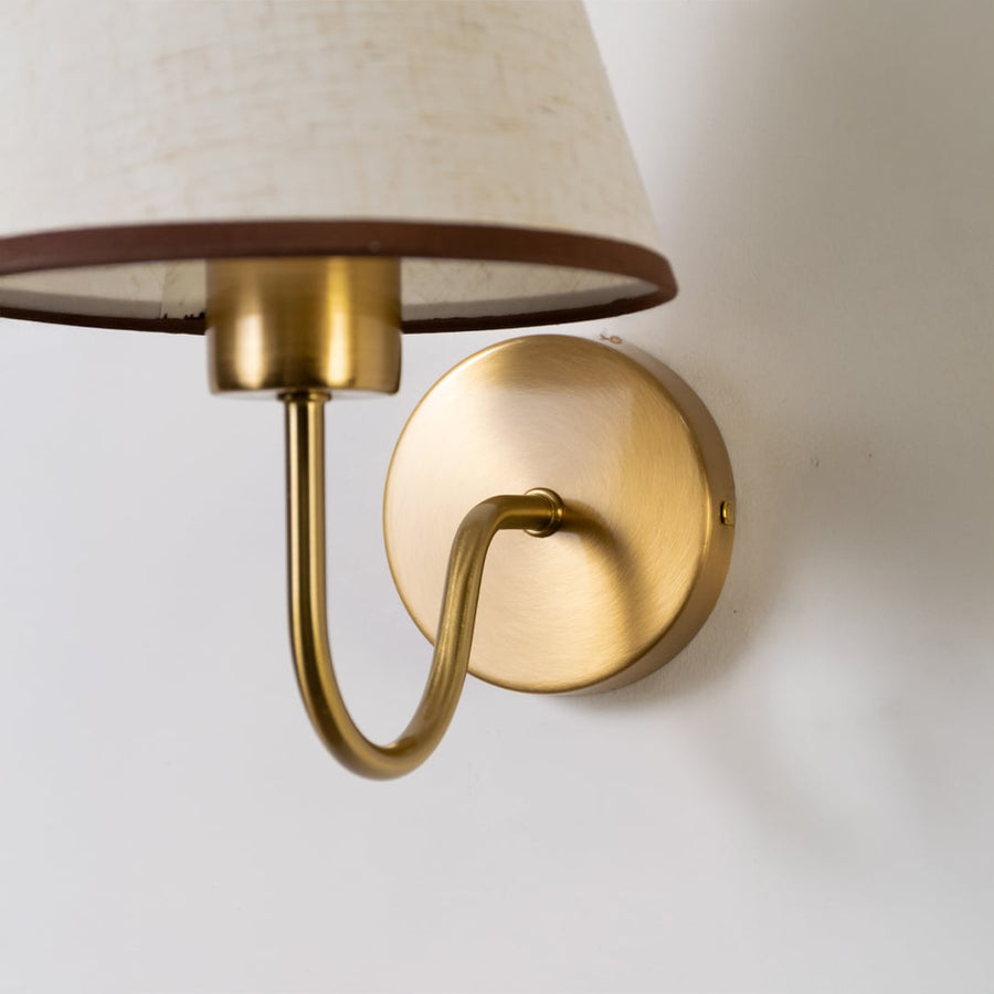 Closeup of gold wall sconce with beige fabric shade showing refined texture and premium modern lighting detail.