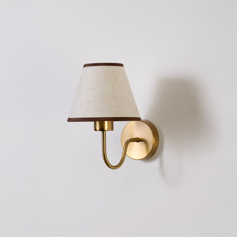Gold metal wall sconce with beige fabric shade shown switched off on white background for minimal elegant wall decor.