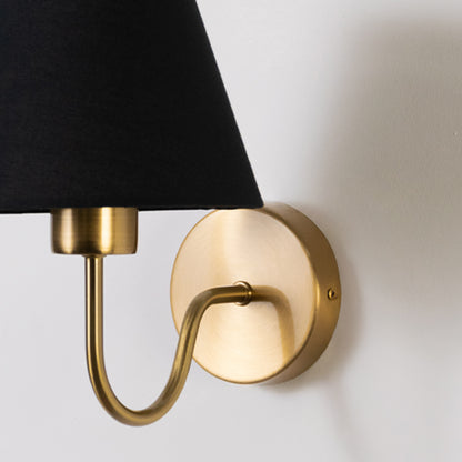 Closeup wall light in gold metal finish with black fabric shade for bedroom or living room decor lighting white background.