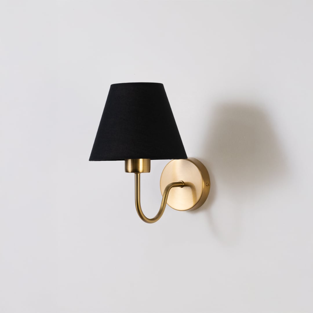 Gold metal wall sconce with black fabric shade shown switched off on white background for minimal stylish wall decor.