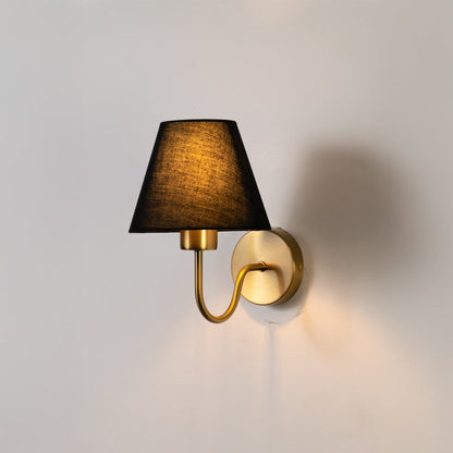 Gold metal wall sconce with black fabric shade glowing softly on white background for elegant modern home decor lighting.