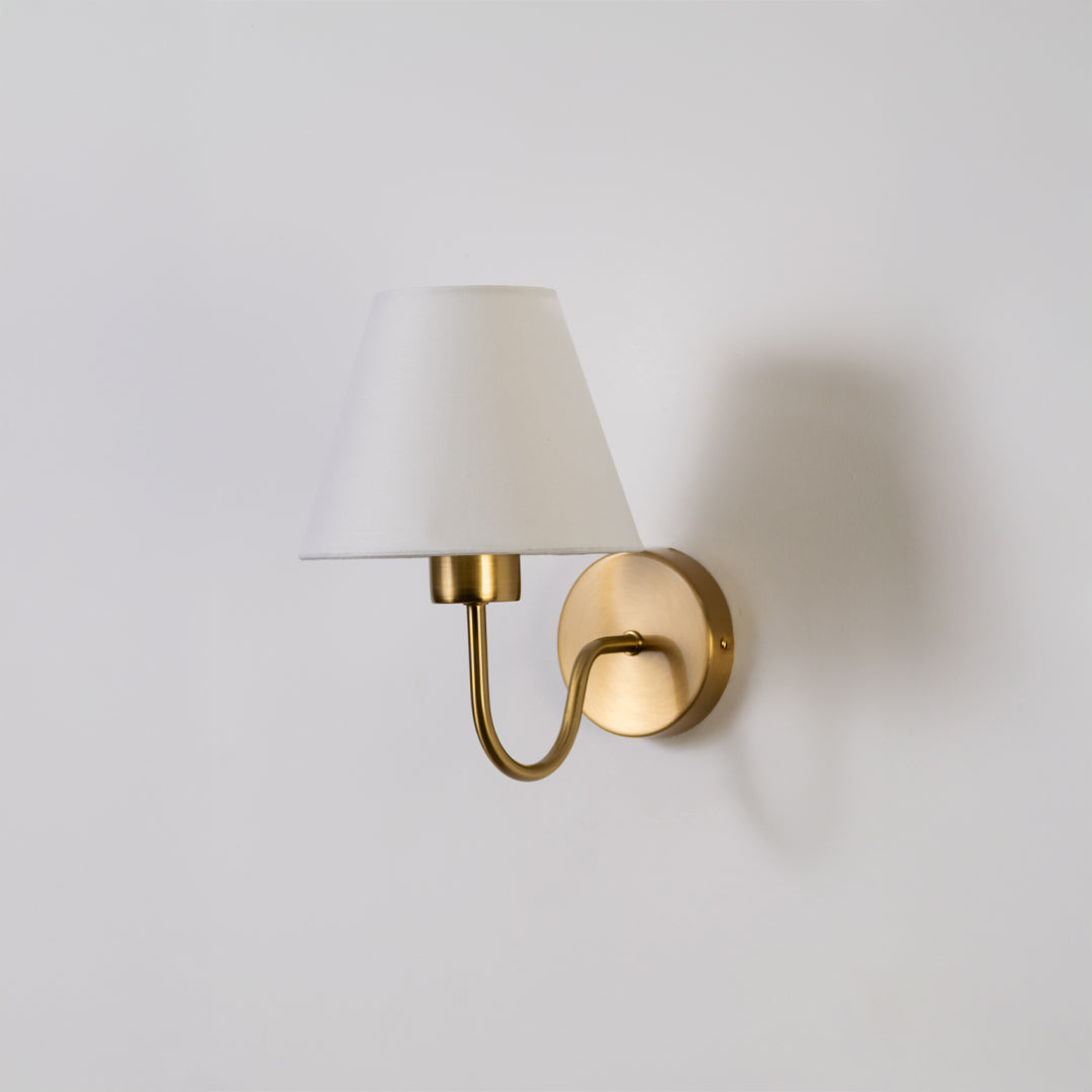 Modern wall light in gold metal finish with white fabric shade for bedroom or living room decor lighting white background.