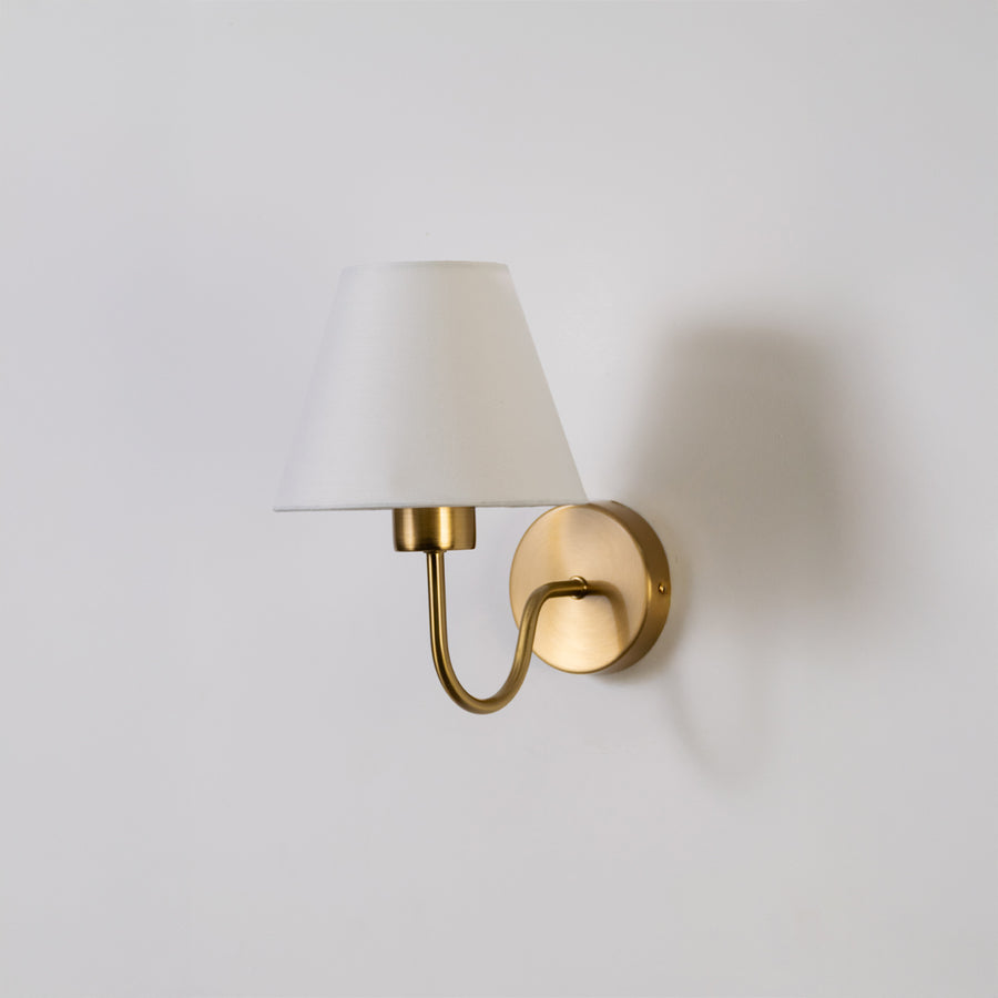 Modern wall light in gold metal finish with white fabric shade for bedroom or living room decor lighting white background.