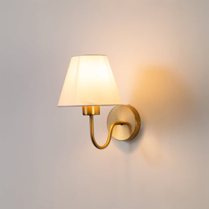 Elegant wall light glowing softly on a white background with a classic fabric shade and warm metal base creating a clean modern look.