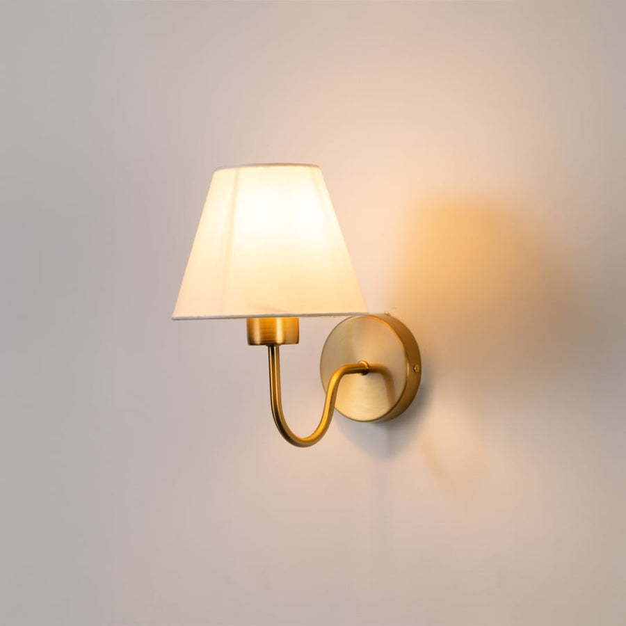 Elegant wall light glowing softly on a white background with a classic fabric shade and warm metal base creating a clean modern look.