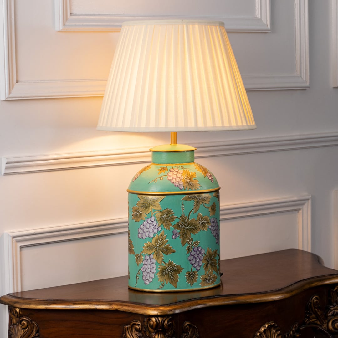 Table lamp on white background featuring a turquoise ceramic base with hand painted floral motifs complemented by a pleated fabric lampshade.