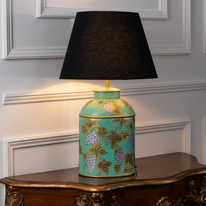 Table lamp on white background highlighting turquoise ceramic base with floral vine detailing finished with a black fabric lampshade.