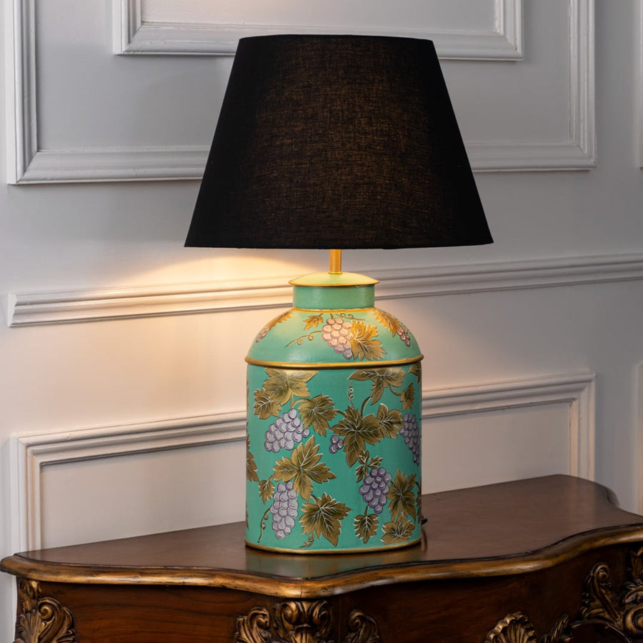 Table lamp on white background highlighting turquoise ceramic base with floral vine detailing finished with a black fabric lampshade.