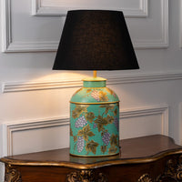 Table lamp on white background highlighting turquoise ceramic base with floral vine detailing finished with a black fabric lampshade.