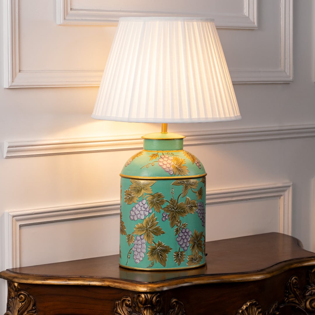 Table lamp with a white pleated shade and turquoise ceramic base featuring hand painted floral motifs styled on a wooden table.