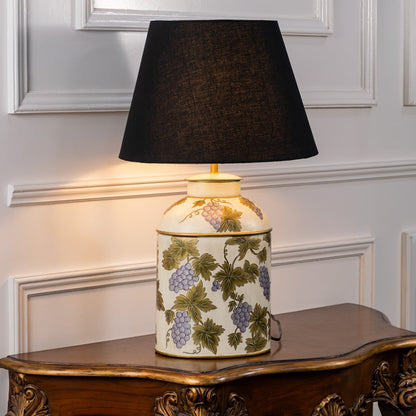 Table lamp on white background featuring ivory ceramic base with green botanical pattern styled with a black fabric lampshade.