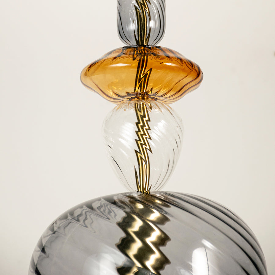 Closeup Image of amber glass pendant light with gold metal accents and twisted cord for elegant ceiling lighting decor.