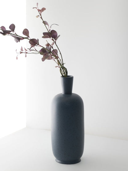 Tall grey ceramic vase with speckled surface styled with purple leaves for elegant modern home decoration.