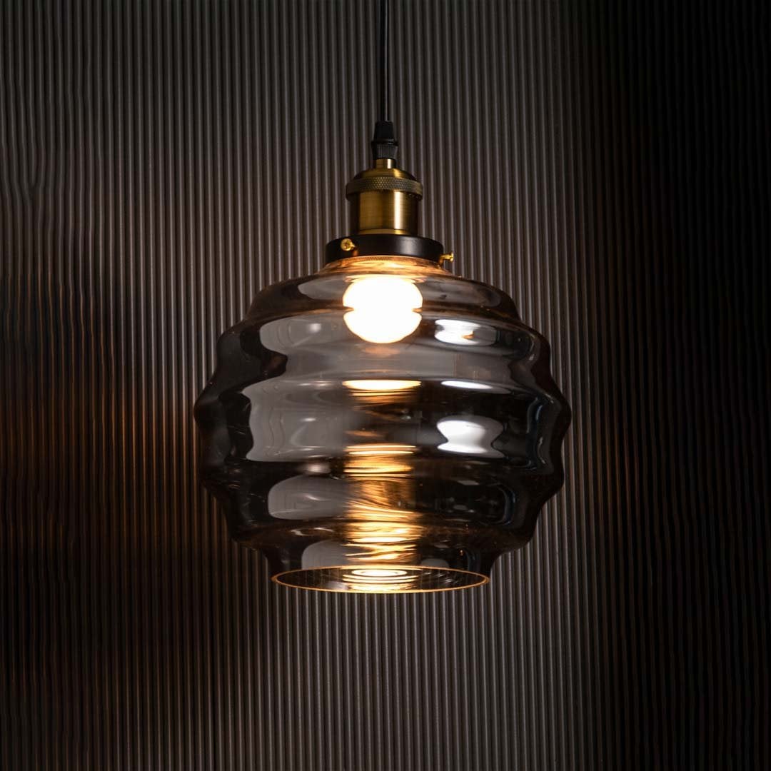 Rippled smoked glass pendant light glowing on a black background enhancing the contrast between the warm illumination and the reflective textured glass surface.