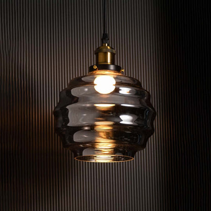 Rippled smoked glass pendant light glowing on a black background enhancing the contrast between the warm illumination and the reflective textured glass surface.