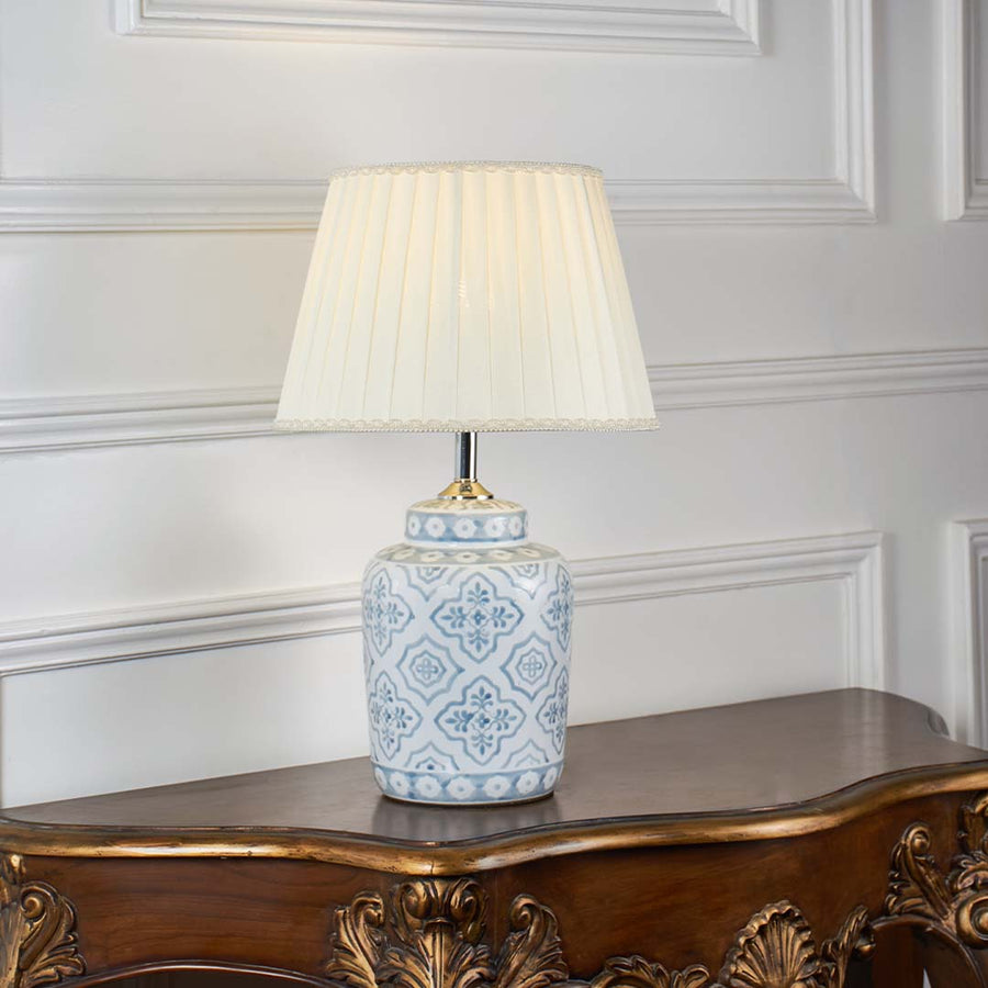 Stylish ceramic table lamp with intricate blue motifs and beige pleated shade turned off on white background showcasing timeless handcrafted appeal.