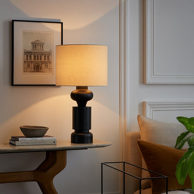 Green ceramic table lamp with beige shade on wooden side table beside a grey sofa in a modern living room.