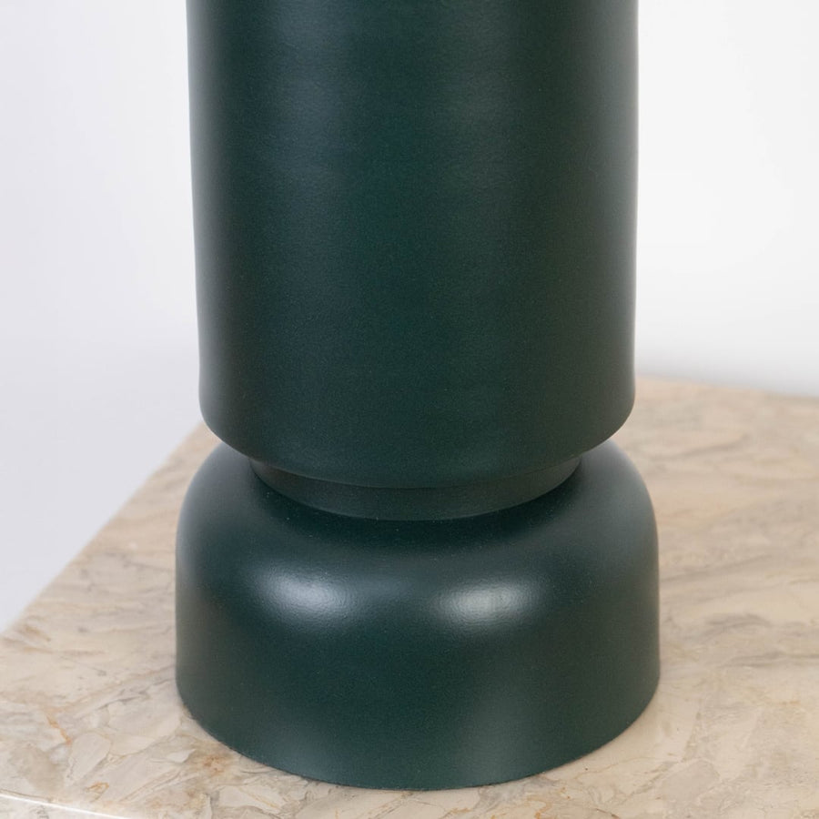 Smooth matte dark green ceramic base of table lamp shown in close-up detail on a marble surface.