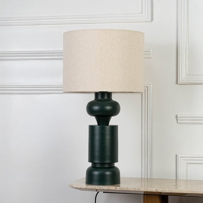 Modern table lamp with dark green ceramic body and cream fabric lampshade isolated on white background.