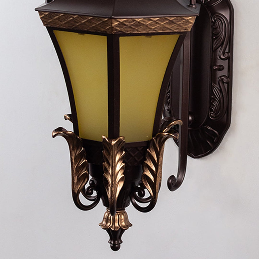Closeup of outdoor wall light with decorative gold leaf design and yellow glass ideal for stylish exterior lighting.