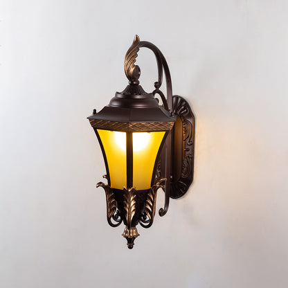 Antique bronze metal outdoor wall light on white background with glowing warm amber glass shade for porch decor.