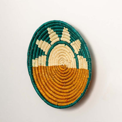 A side angle view of the teal mustard and natural rattan wall decor plate showing its raised woven rim and detailed handcrafted texture for warm colorful home styling.
