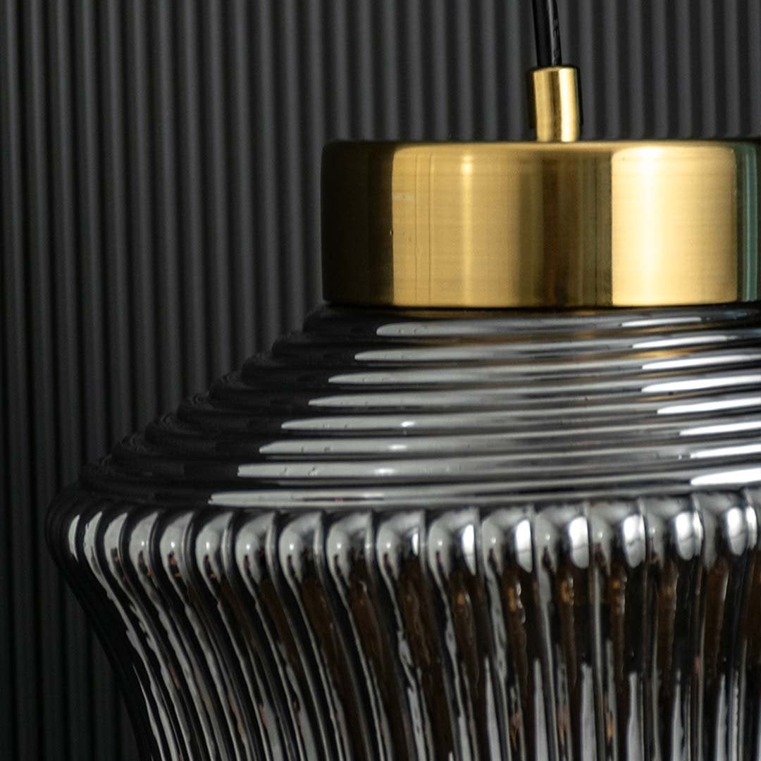 Closeup of ribbed smoked glass pendant light capturing its textured curved surface brass top detail and modern reflective finish for stylish decor.