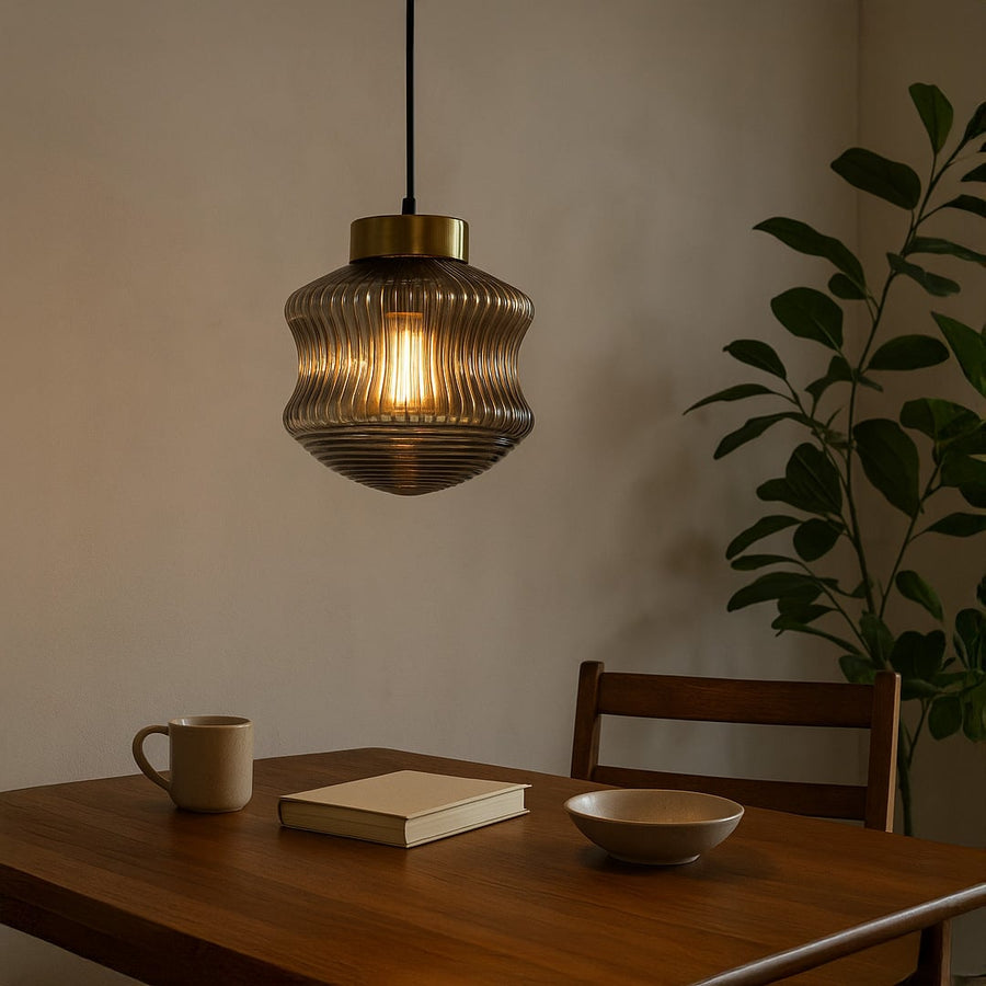 Ribbed smoked glass pendant light with warm glowing bulb hanging above a wooden dining table creating a cozy modern atmosphere in a neutral interior.