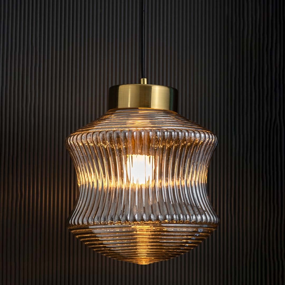 Smoked ribbed glass pendant light displayed with light on against a dark backdrop enhancing its warm illumination and decorative modern form.