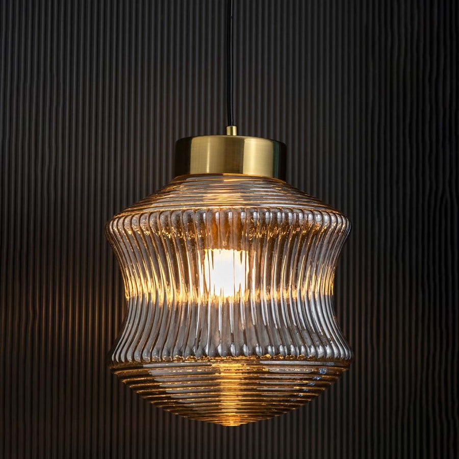 Smoked ribbed glass pendant light displayed with light on against a dark backdrop enhancing its warm illumination and decorative modern form.