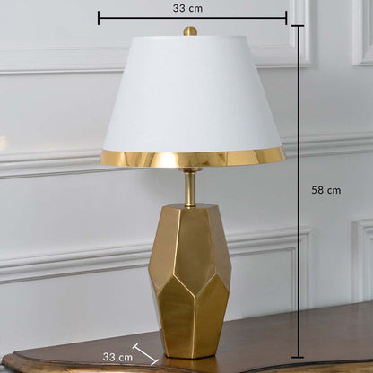Gold geometric table lamp with white tapered shade shown with dimensions of 33 cm width 58 cm height and 33 cm depth ideal for bedside or console placement.