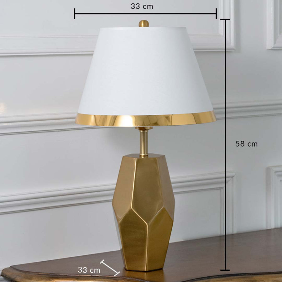 Gold geometric table lamp with white tapered shade shown with dimensions of 33 cm width 58 cm height and 33 cm depth ideal for bedside or console placement.