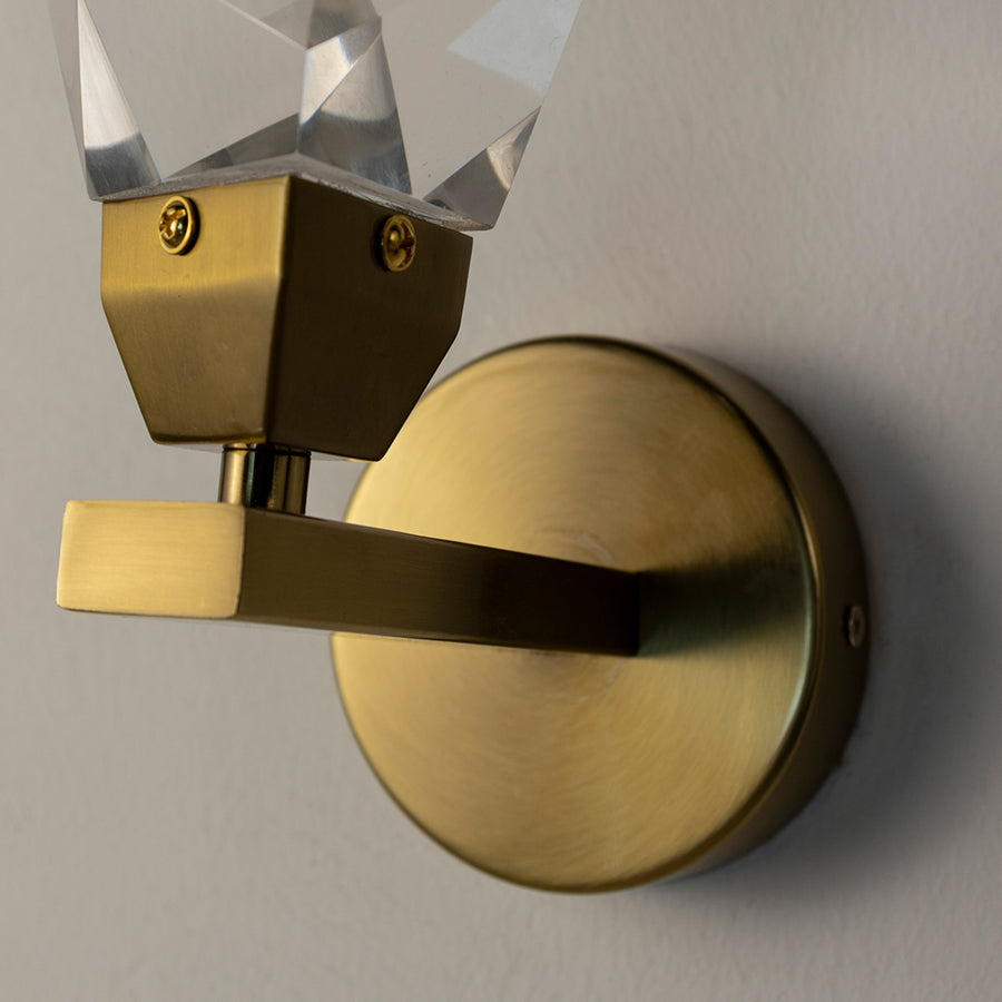 Contemporary brass wall light with faceted crystal glass shade for luxury modern interior decor.
