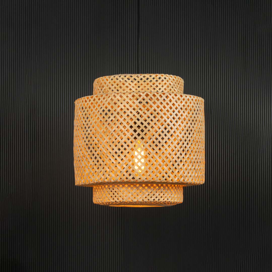 Handwoven rattan pendant light with layered bamboo shade turned on glowing softly against black background.