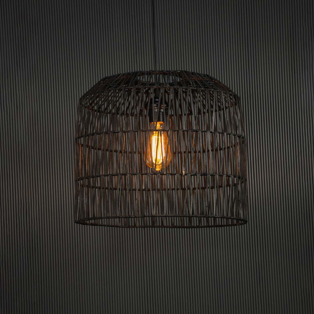 Black handcrafted wire pendant lamp glowing on dark background radiating a soft warm light through intricate geometric weave.