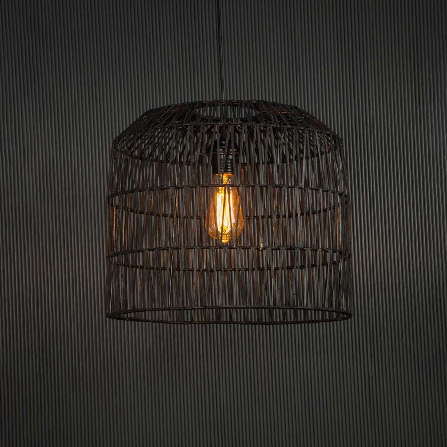 Black handcrafted wire pendant lamp glowing on dark background radiating a soft warm light through intricate geometric weave.