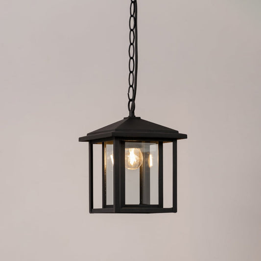 Black metal outdoor hanging lantern with glass panels illuminated on a white background for a clean product display.