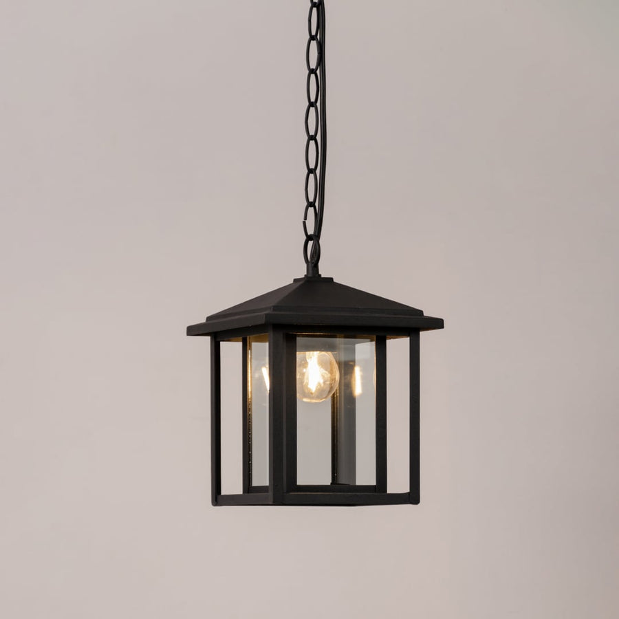 Black metal outdoor hanging lantern with glass panels illuminated on a white background for a clean product display.