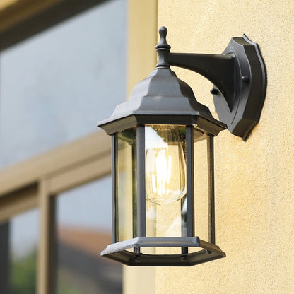 A decorative outdoor wall lantern with the light on mounted near a doorway casting a soft ambient glow on the wall and enhancing the natural greenery around the entrance.