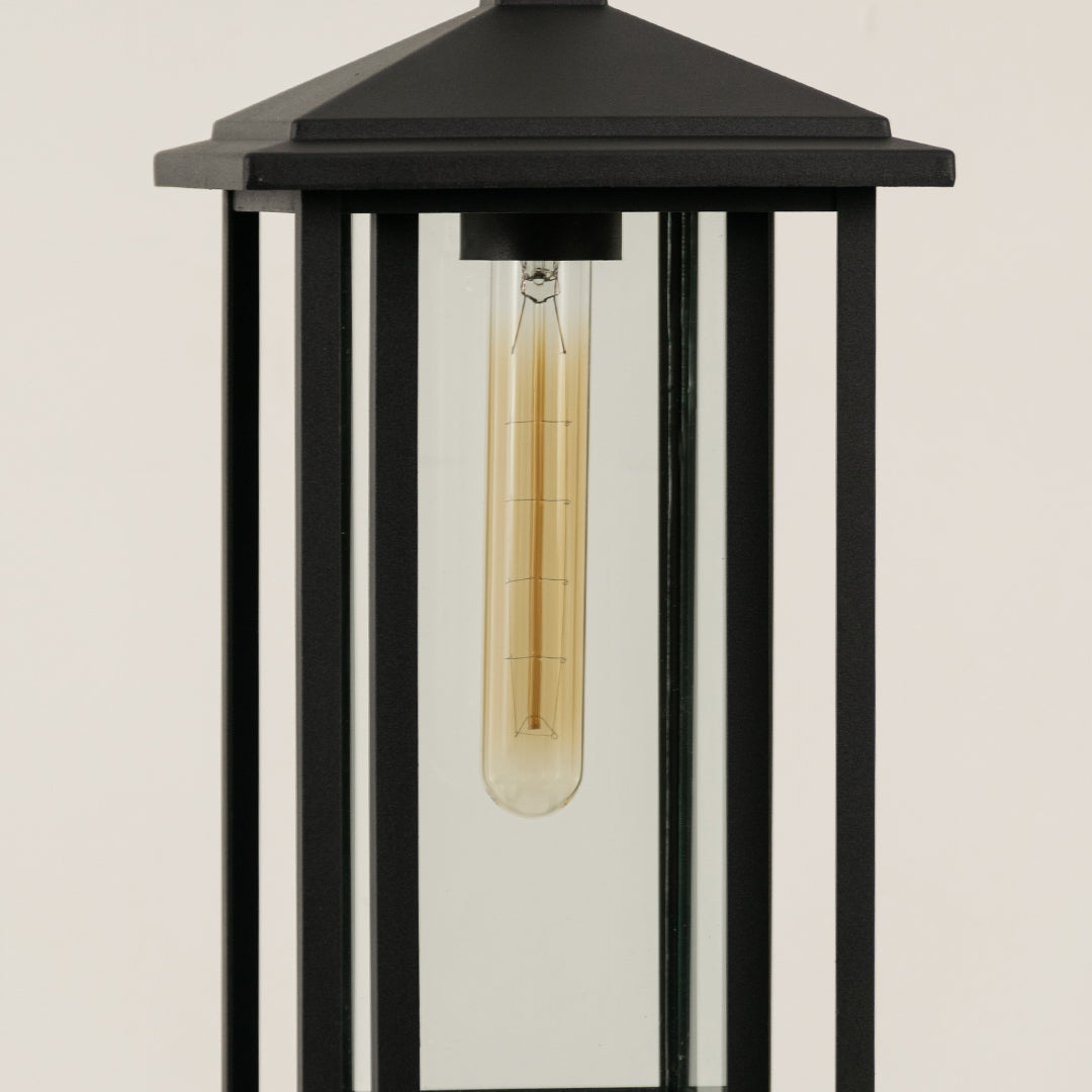 Closeup of black metal outdoor lantern with clear glass panels and bulb on white background perfect for modern exterior decor lighting.