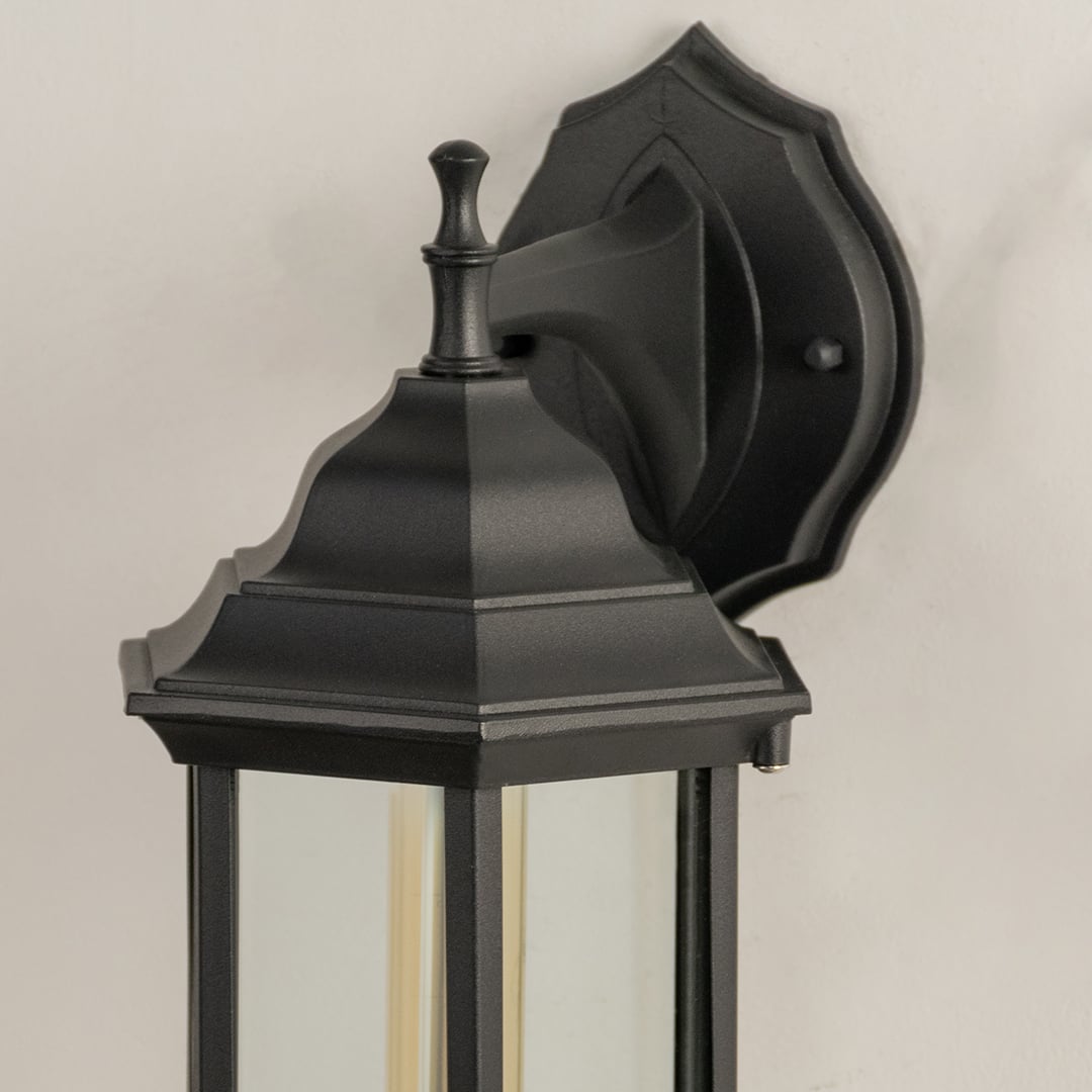 A closeup of the outdoor wall lantern showing the clear glass panels and glowing bulb with detailed metal edges highlighting the lantern’s classic architectural styling.