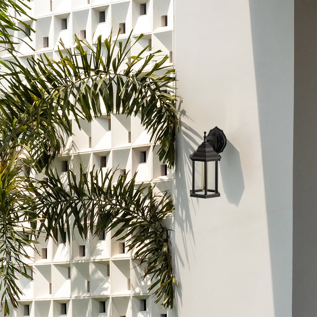 A decorative outdoor wall lantern with the light on Outdoor wall near a doorway casting a soft ambient glow on the wall and enhancing the natural greenery around the entrance.